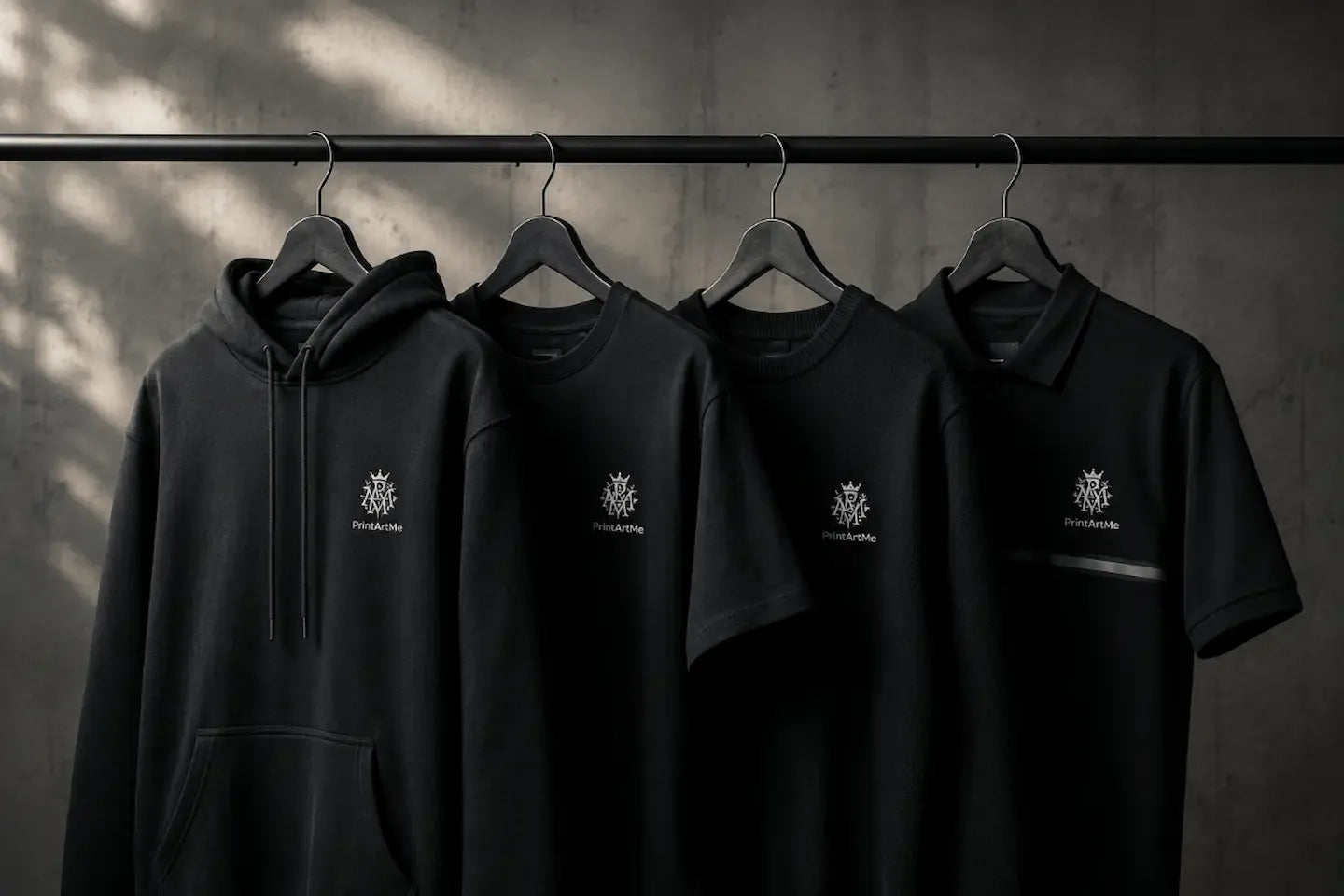 Black hoodies and t-shirts with a logo on hangers against a dark background